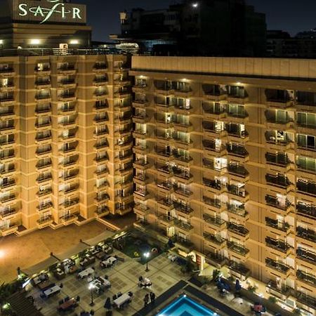 โรงแรมซาเฟอไคโร Giza ภายนอก รูปภาพ The photo shows a multi-story hotel building at night. The building is illuminated, showcasing multiple balconies along its facade. In front of the hotel, there is an outdoor area with seating arranged around a pool, which is also lit up. The hotel's