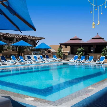 โรงแรมซาเฟอไคโร Giza ภายนอก รูปภาพ The photo showcases a bright, inviting swimming pool surrounded by lounging chairs. The pool is set in a sunny outdoor area, with clear blue water reflecting the sky. There are several blue umbrellas providing shade over the lounge chairs, which are 