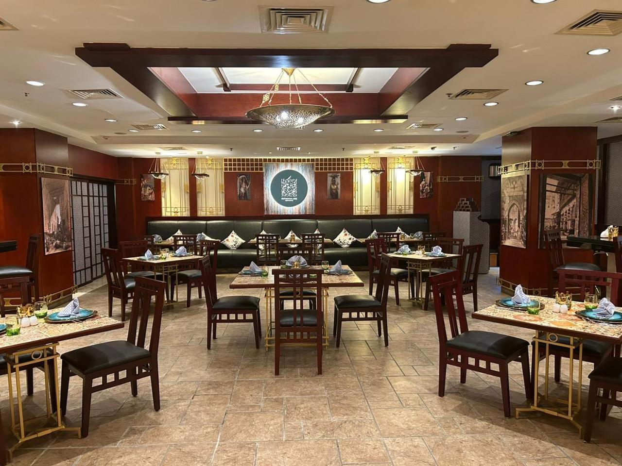 โรงแรมซาเฟอไคโร Giza ภายนอก รูปภาพ The photo shows the interior of a restaurant. The space features a combination of warm wood tones and elegant decorations. There are several dining tables arranged throughout, each set with plates, cutlery, and decorative napkins. The walls are adorn