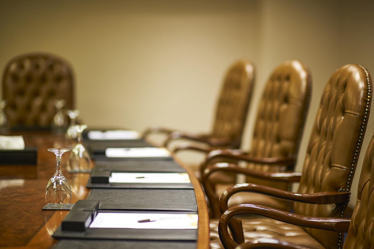 โรงแรมซาเฟอไคโร Giza ภายนอก รูปภาพ The photo shows a conference room setting with a long wooden table and several high-backed chairs. The chairs appear to be upholstered in a brown leather material. Each place at the table has a black folder or pad, and there are also glass water gobl