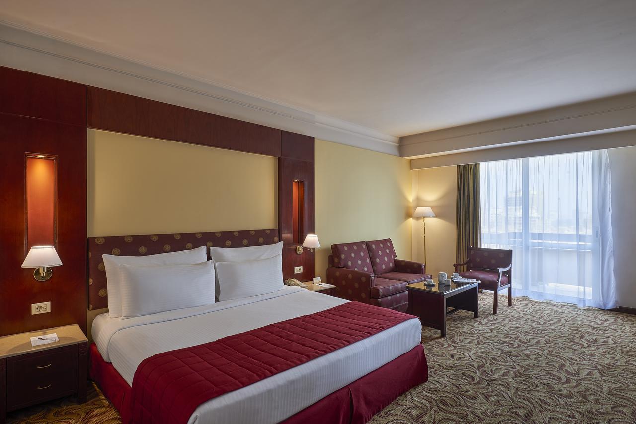 โรงแรมซาเฟอไคโร Giza ภายนอก รูปภาพ The image showcases a hotel room featuring a large bed with white linens and a red bedspread. Behind the bed, there is a decorative headboard. The room includes two armchairs and a small coffee table, creating a seating area. Natural light enters thr