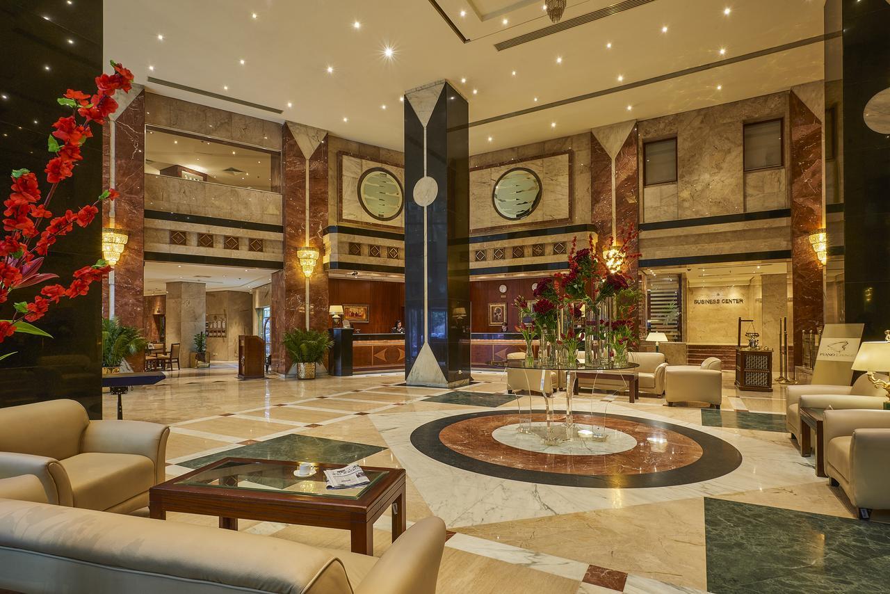 โรงแรมซาเฟอไคโร Giza ภายนอก รูปภาพ The photo shows a luxurious hotel lobby. The space features elegant marble flooring with a circular design at the center. There are comfortable seating arrangements with light-colored sofas and wooden coffee tables. Lush green plants and vibrant flor