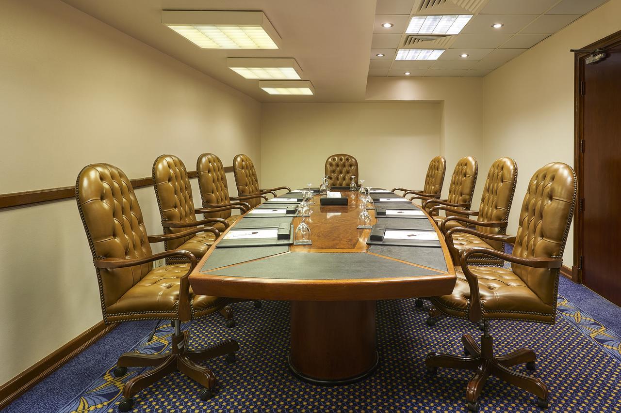 โรงแรมซาเฟอไคโร Giza ภายนอก รูปภาพ The photo shows a conference room with a large oval table surrounded by several brown leather chairs. There are eight chairs in total, each with a high back and wheels. The table has some notepads and glasses of water set up on it. The room has neutr