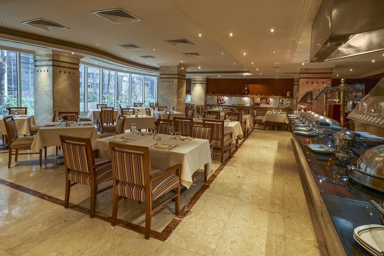 โรงแรมซาเฟอไคโร Giza ภายนอก รูปภาพ The photo shows the interior of a restaurant. It features a spacious dining area with several tables laid out with white tablecloths. The tables are accompanied by wooden chairs that have striped patterns. The restaurant is well-lit with soft lightin