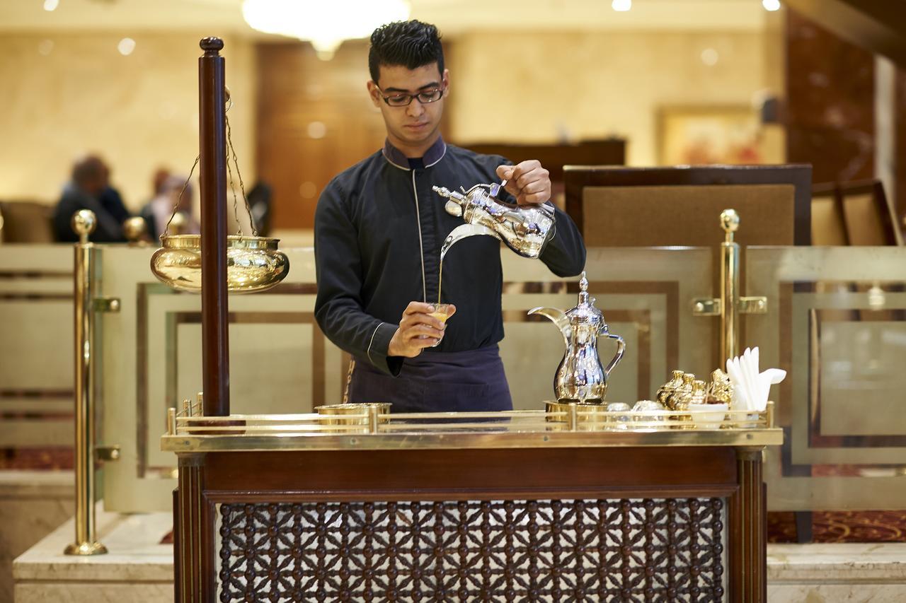 โรงแรมซาเฟอไคโร Giza ภายนอก รูปภาพ The photo depicts a person at a service counter, pouring tea from a traditional teapot. The individual appears to be dressed in a formal, dark outfit, and is focused on the task of pouring. The counter features ornate decorations and various tea-serv
