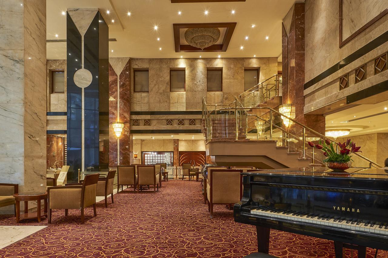 โรงแรมซาเฟอไคโร Giza ภายนอก รูปภาพ The image shows an elegant hotel lobby. The space features marble walls and a plush carpet, giving it a luxurious feel. There are seating areas with comfortable chairs arranged around tables. A grand staircase leads to an upper level, and large windo