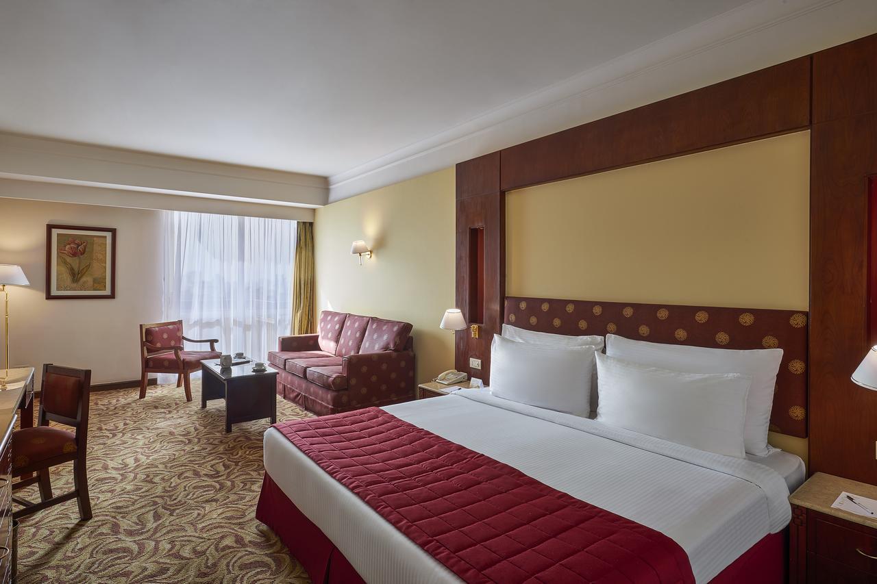 โรงแรมซาเฟอไคโร Giza ภายนอก รูปภาพ The photo shows a hotel room featuring a spacious layout. In the center, there is a large bed with white bedding and a red decorative coverlet. To one side, there is a seating area that includes a sofa and two armchairs, all set around a small coffee