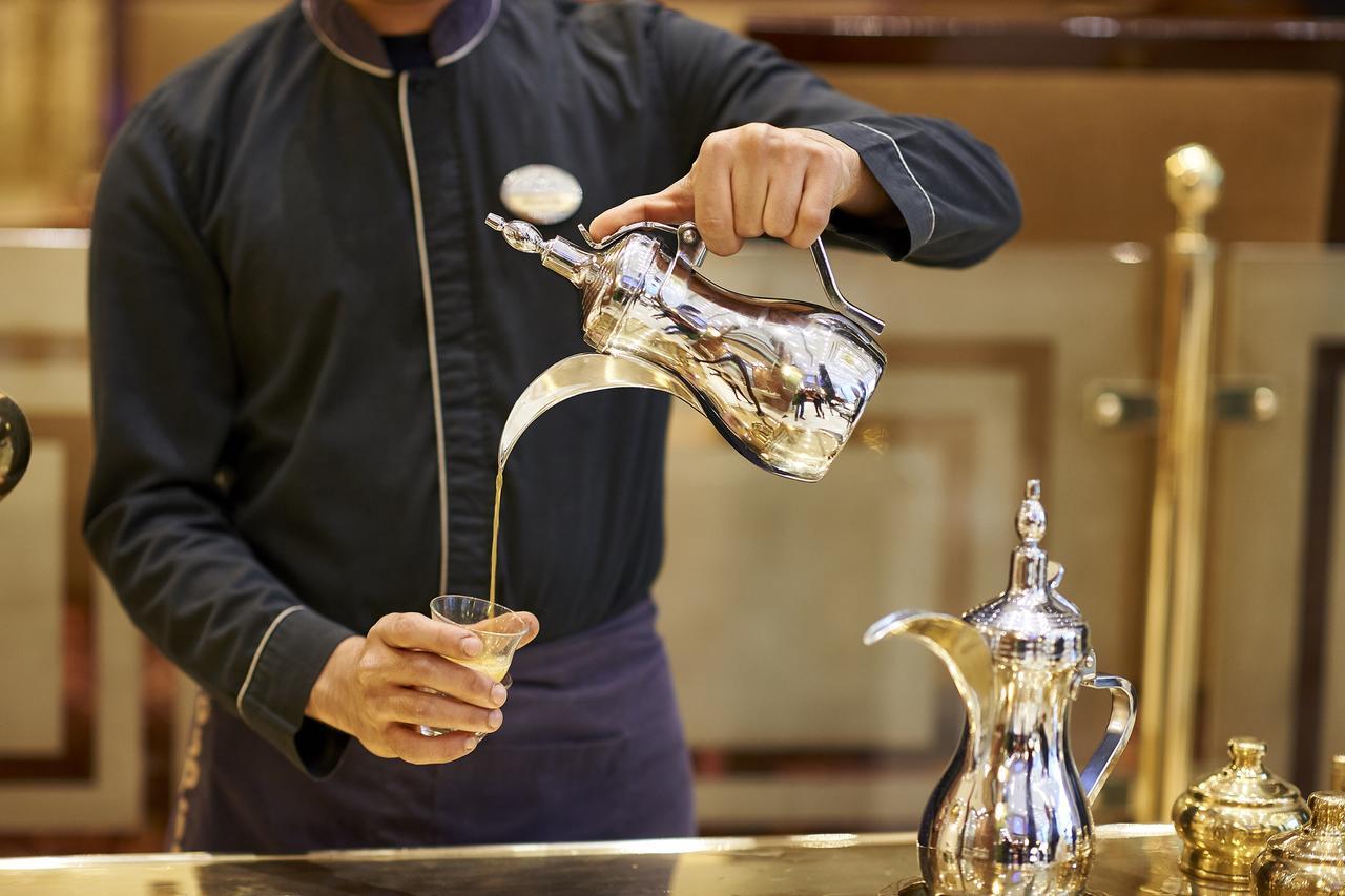 โรงแรมซาเฟอไคโร Giza ภายนอก รูปภาพ The image shows a server pouring a beverage from a shiny silver teapot into a glass. The server is wearing a dark uniform and has a focused expression. The teapot is intricately designed, and there is another similar pot alongside it on the counter. 
