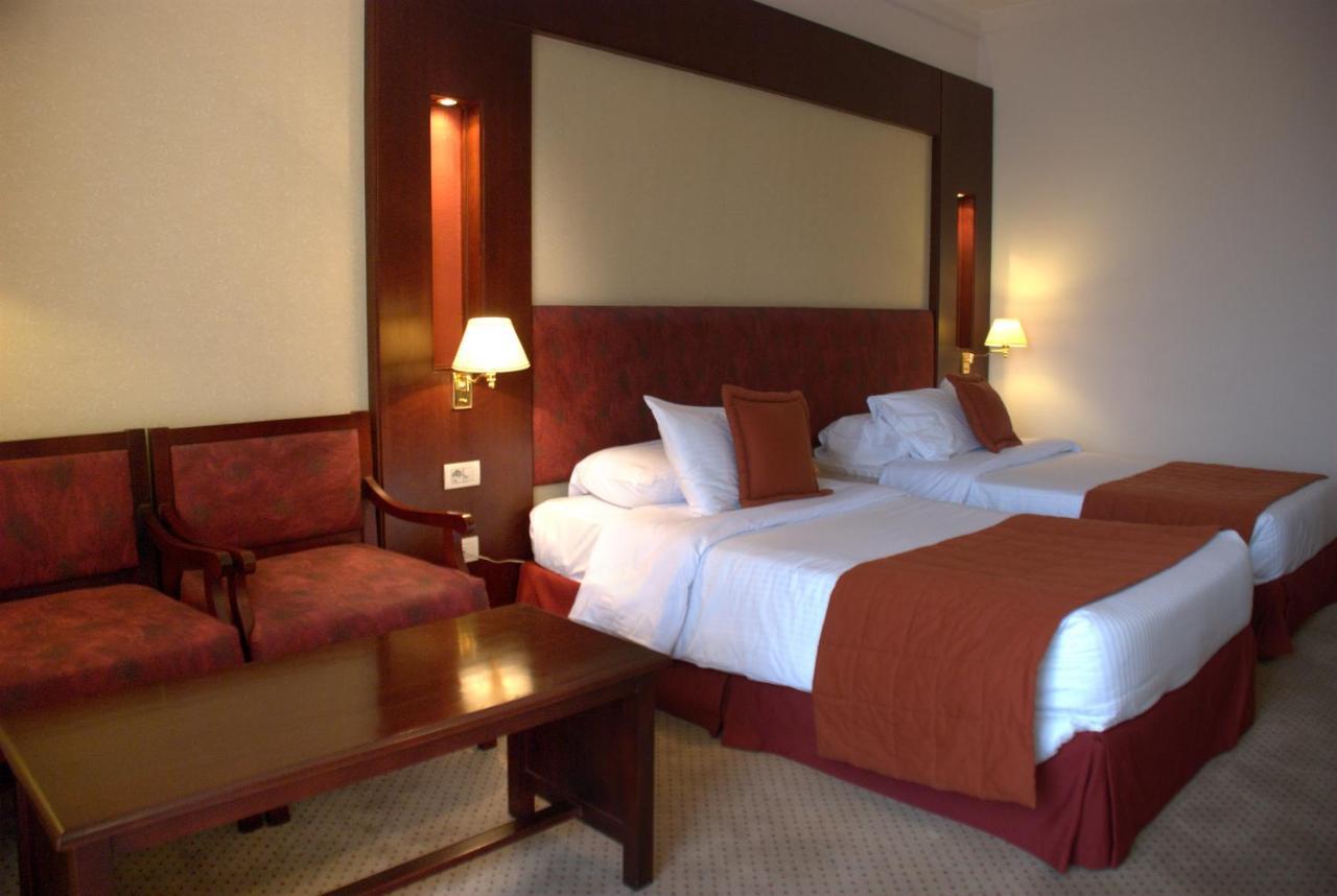 โรงแรมซาเฟอไคโร Giza ภายนอก รูปภาพ The photo shows a hotel room featuring two twin beds with white linens and orange bedspreads. There is a headboard behind the beds, along with wall-mounted lamps on either side. In the corner, there are two upholstered chairs and a wooden coffee tabl