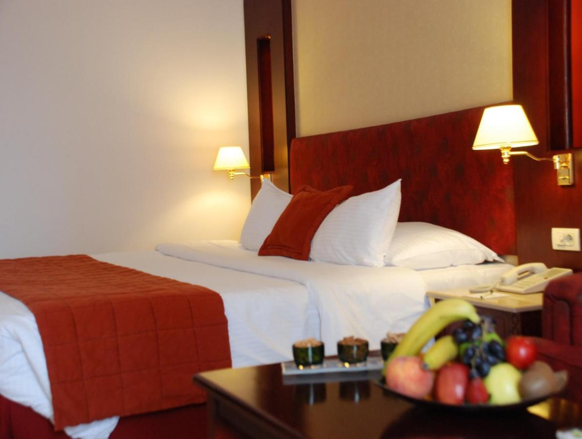 โรงแรมซาเฟอไคโร Giza ห้อง รูปภาพ The photo shows the interior of a hotel room featuring two beds with white bedding and an orange throw blanket. There are decorative pillows on the beds. The walls are designed in warm tones, and there are two bedside lamps providing soft illuminatio