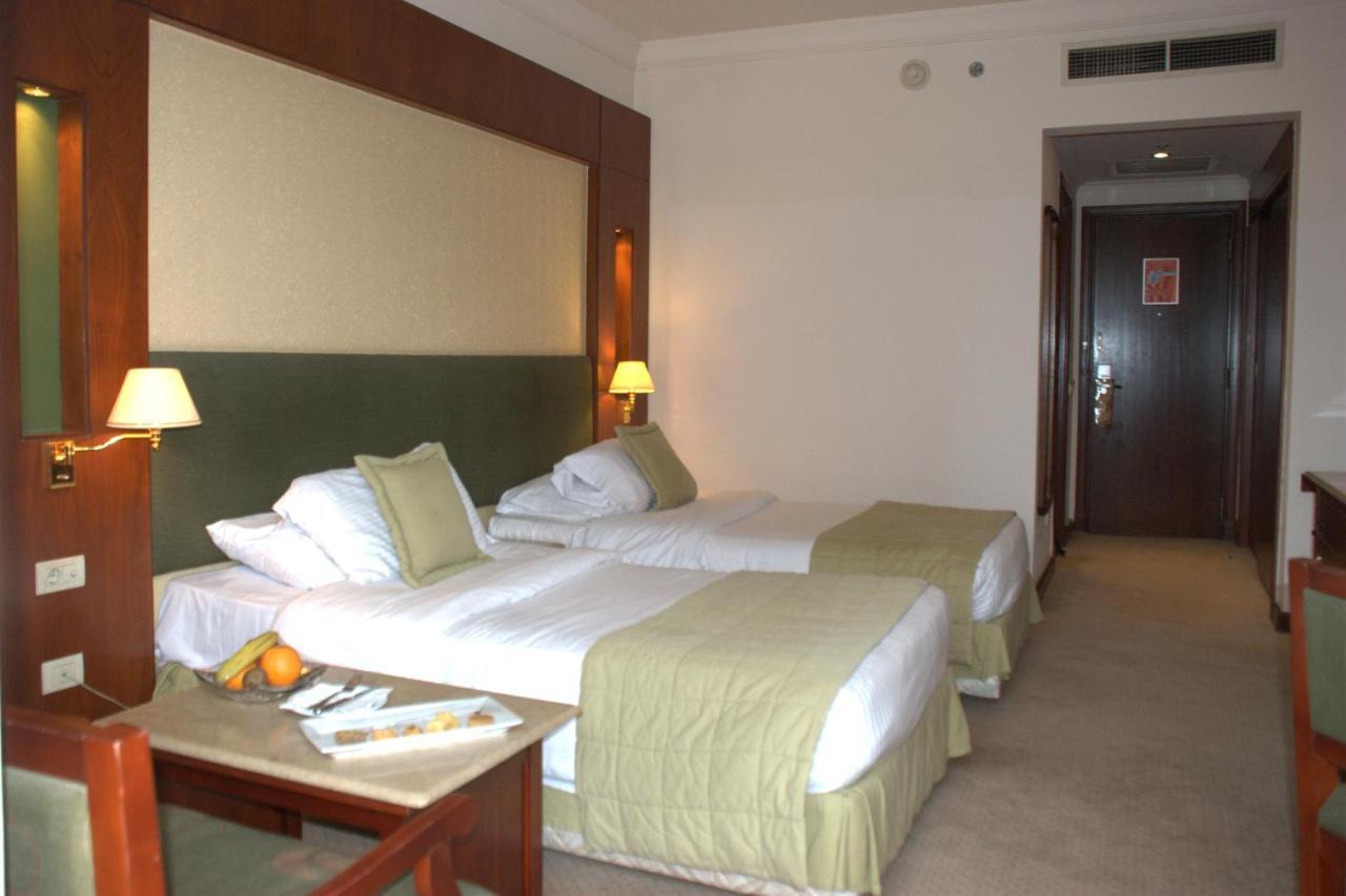 โรงแรมซาเฟอไคโร Giza ห้อง รูปภาพ The photo shows a hotel room featuring two single beds with light green bedspreads and white linens. There are bedside lamps on either side of the beds, and the headboard has a soft, textured design. A small seating area is visible with a wooden chai